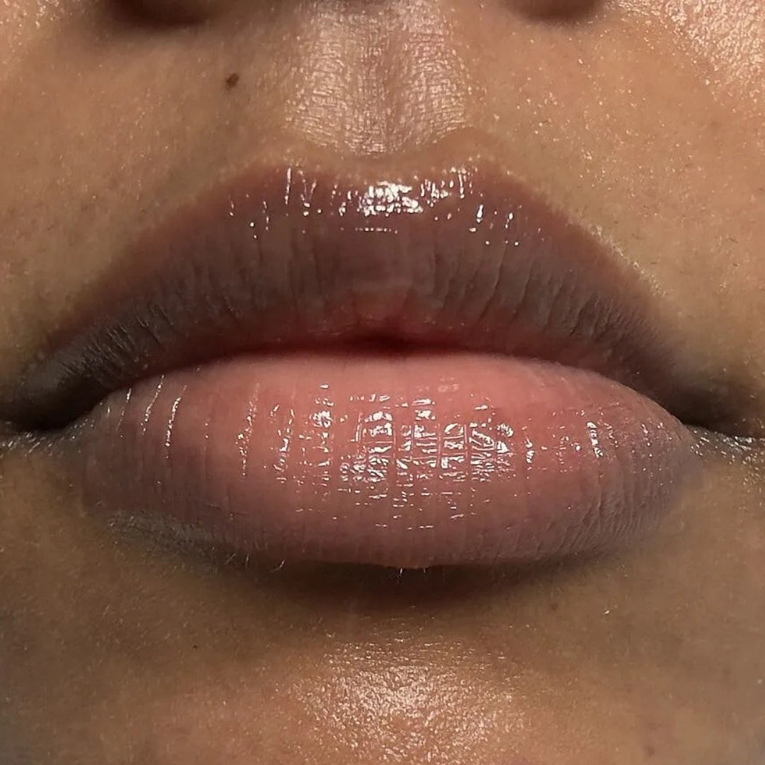 Close-up of a person's lips wearing a glossy, sheer pink lip product with a high-shine finish. Shows the after results of using the frank body barrier protect lip product.