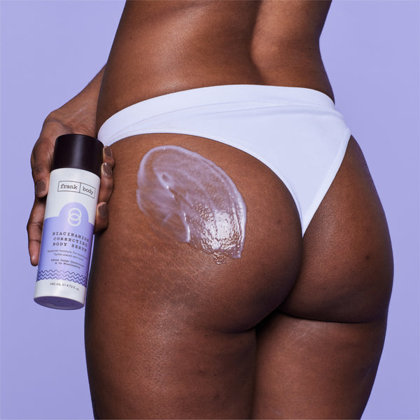 A close-up of a person from the back wearing white underwear, holding a can of Frank Body Cream with a thick white cream swatch applied to the upper buttock against a solid lavender background.