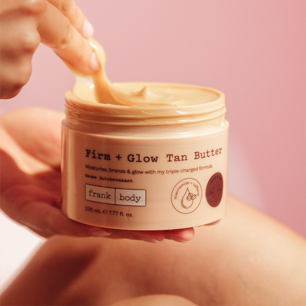 A hand scooping frank body Firm + Glow Tan Butter from the open jar.