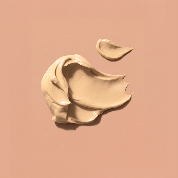 A swirled smear of tanning butter, on a solid warm peach-pink background with a smaller smear above it.