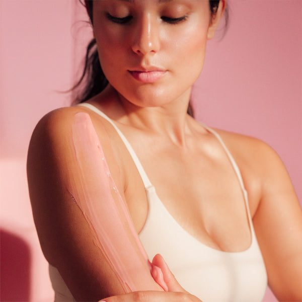 A person with Firming Body Glaze smoothed over their chest and shoulder, against a pink background.