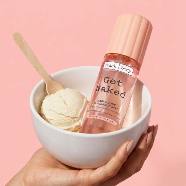 A hand holding a bowl of vanilla ice cream with a bottle of frank body Get Naked Hair & Body Fragrance Mist resting in it.