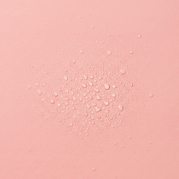 Droplets of frank body Get Naked Hair & Body Fragrance Mist on a pink background.
