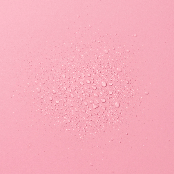 Droplets of frank body Hot Lick Hair & Body Fragrance Mist on a pink background.