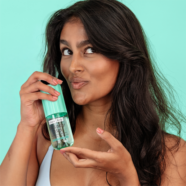 A woman in a pale blue bra holding a bottle of frank body On-the-Go Skinny Dip Hair & Body Fragrance Mist.