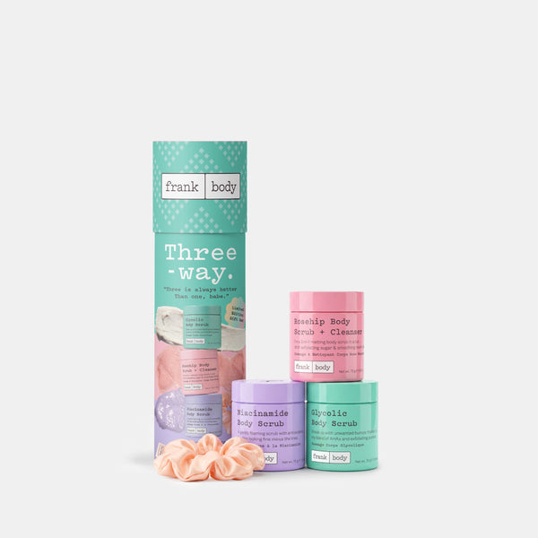 Frank Body Three Way body care set on a light gray background, featuring a mint green cylindrical box, three pastel-colored jars (pink, purple, and teal), and a peach scrunchie.